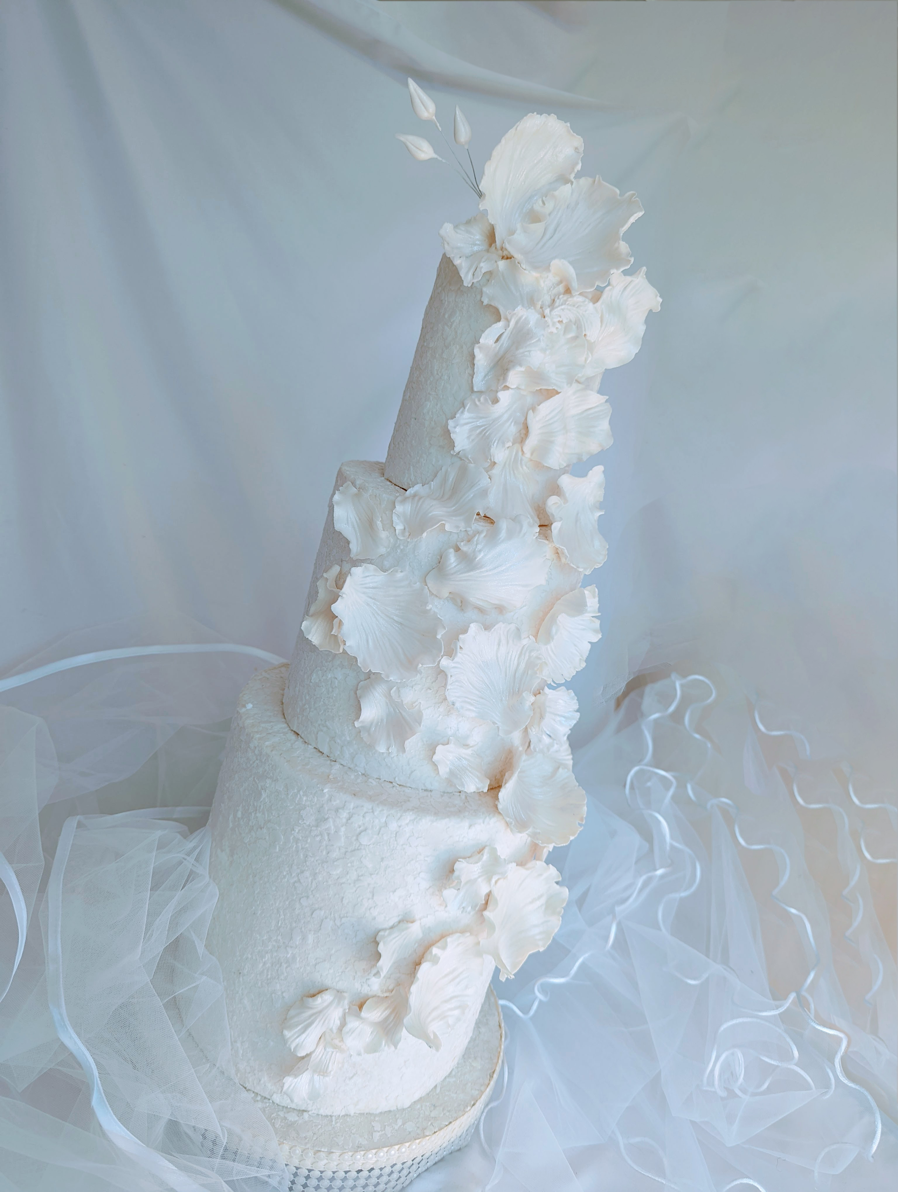 3 tier elegant wedding cake with various flower petals decorating the cake from top to bottom.
